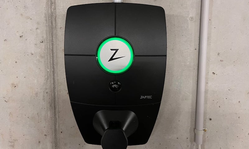 A black Zaptec EV charger against a grey cement wall in a garage